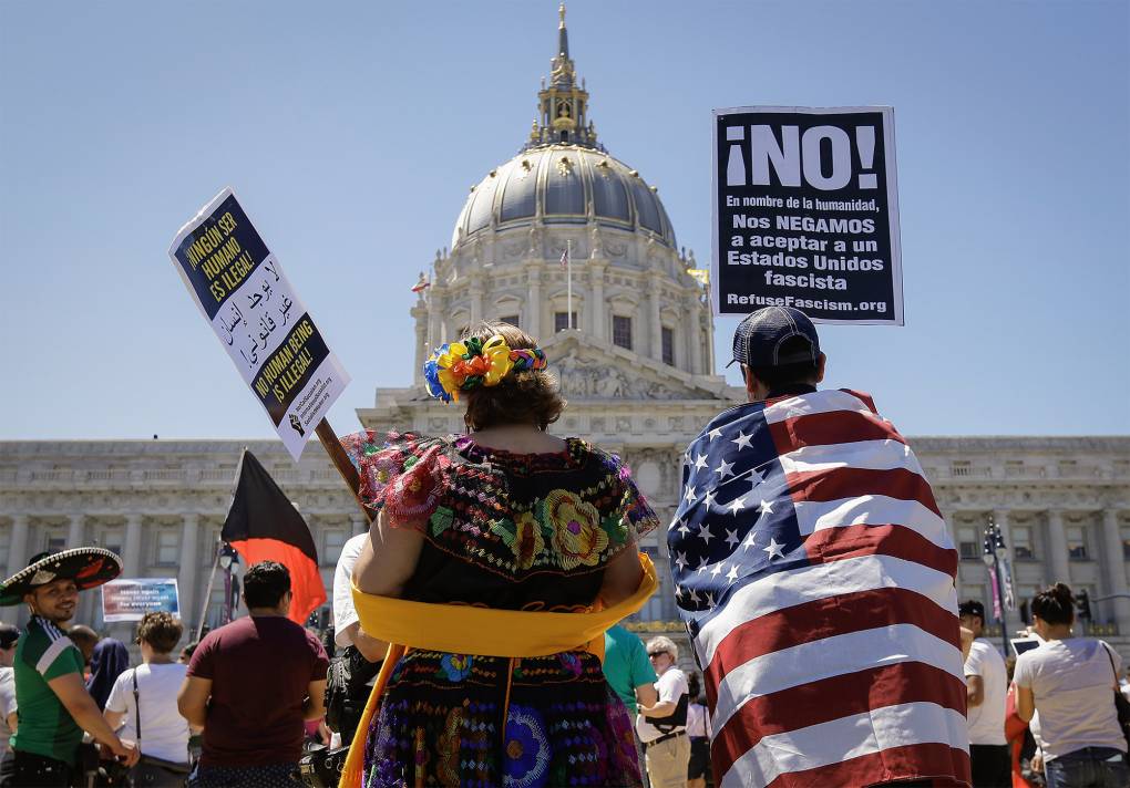 People fill a plaza holding signs in front of a large ornate building.