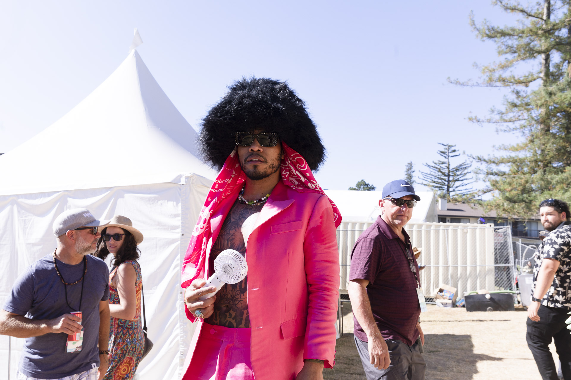 Anderson .Paak poses back stage wearing a pink suit, no shirt and a giant fur hat.