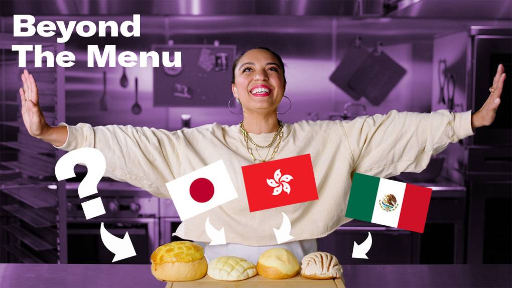 A smiling woman is standing in the kitchen in front of four different sweet buns that each have a flag from their country of origin next to them.