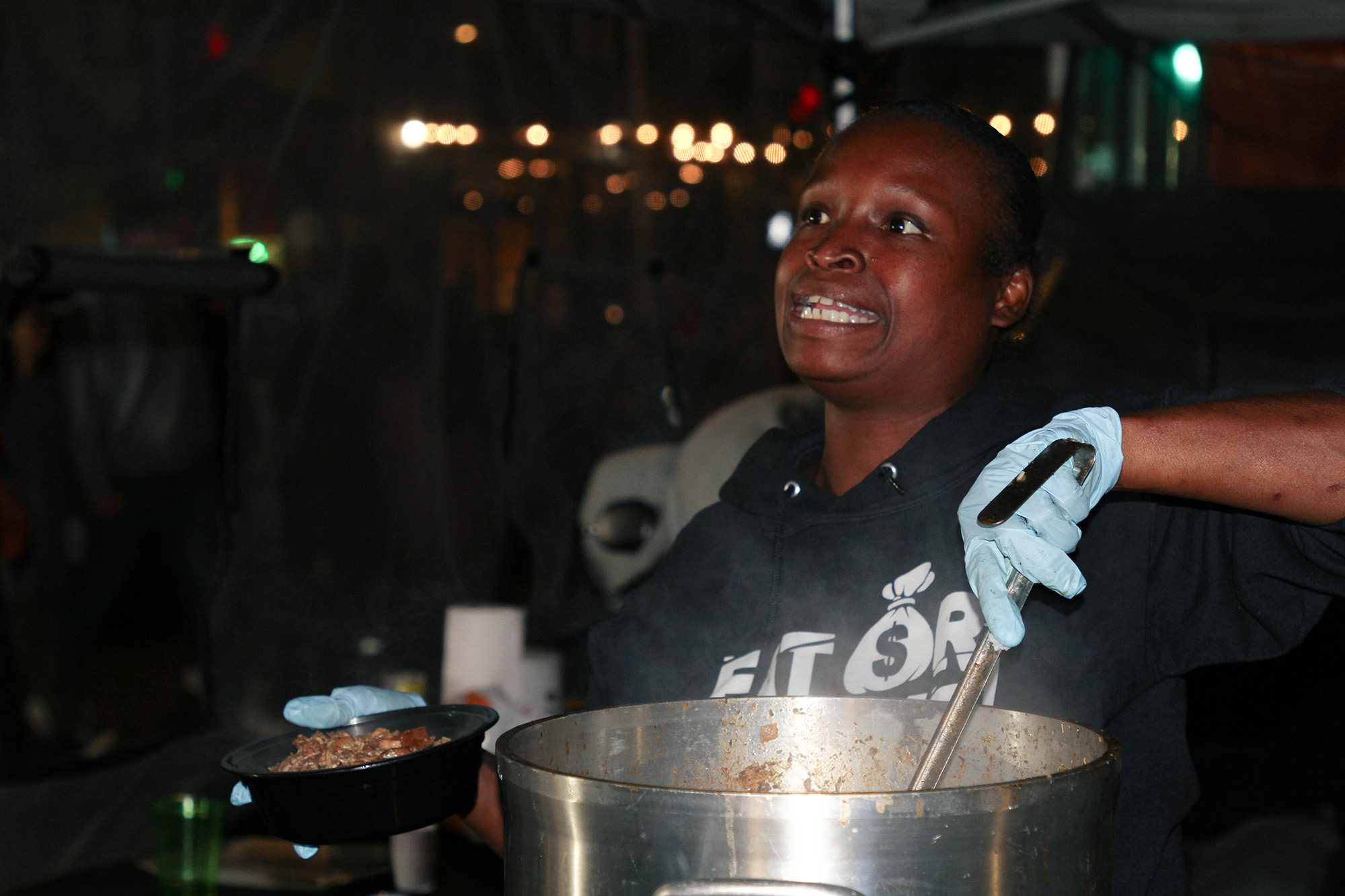 An outdoor vendor ladles stew into a bowl at night.