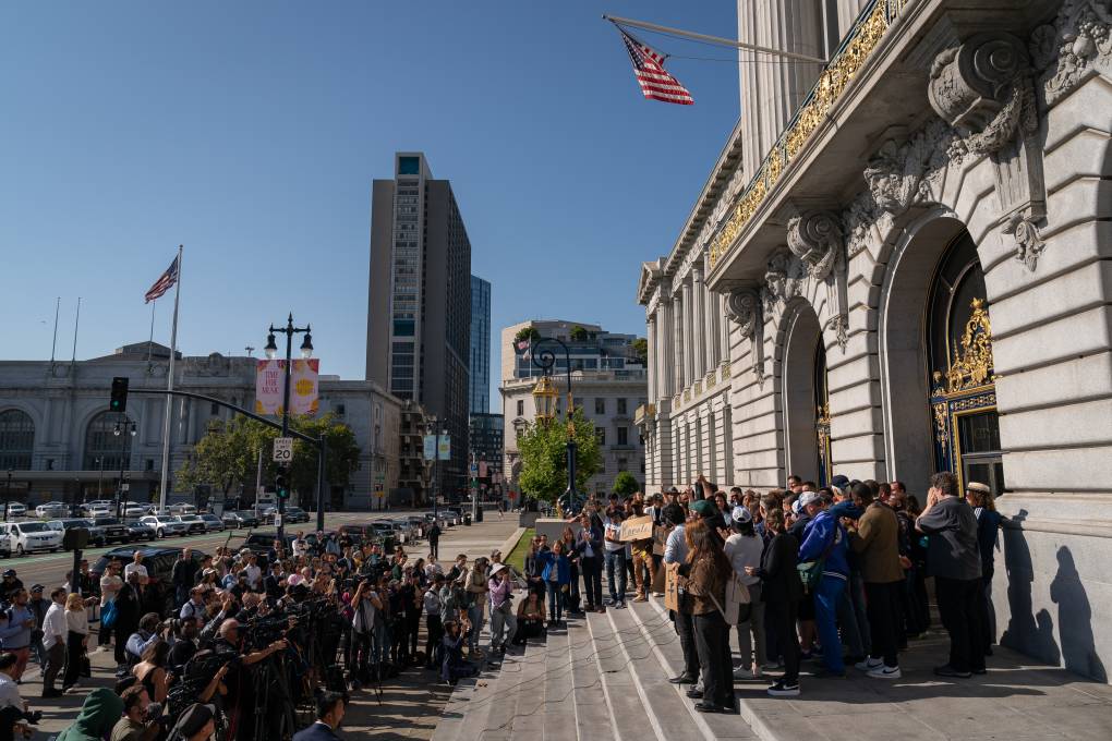 Several people stand in front of SF City Hall under a waving American flag.