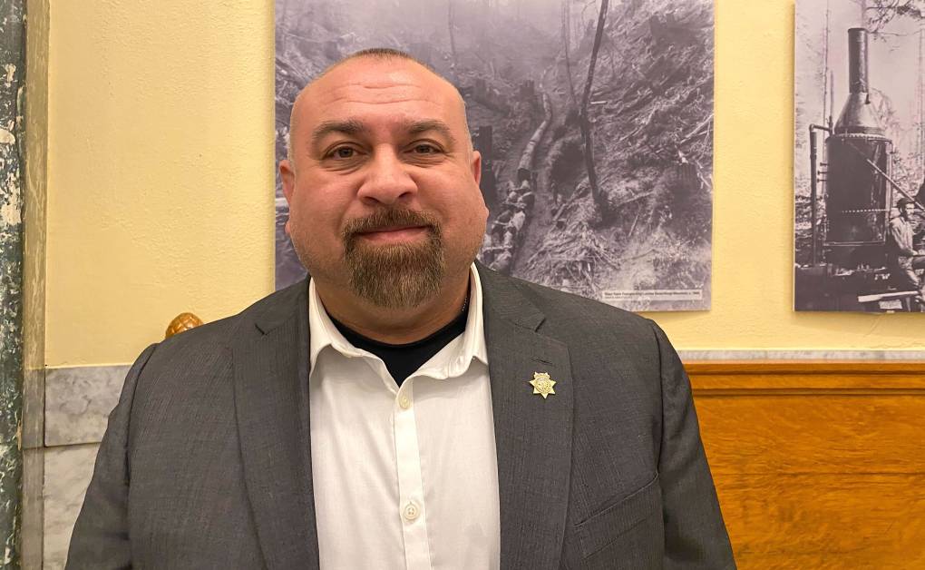 A middle-aged man with a goatee, wearing a sheriff's star pin, poses for a photo.