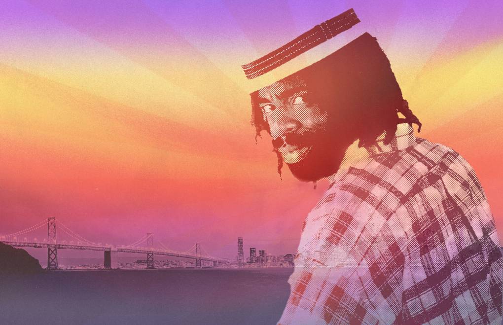 A Black man in a pattered button-up shirt, a fashionable hat and dreadlocks looks over his shoulder as the Bay Bridge stretches out in the background against a color-treated sky