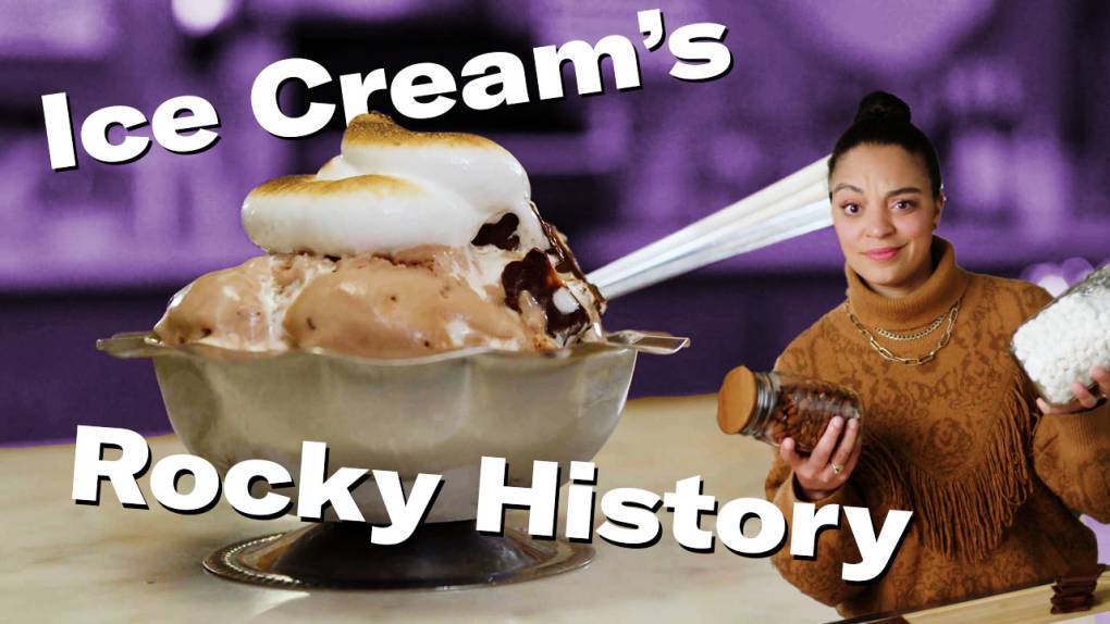 A close-up of a metal serving dish with rocky road ice cream scoops topped with marshmallow fluff next to a woman holding a jar of mini marshmallows and almonds in each hand.