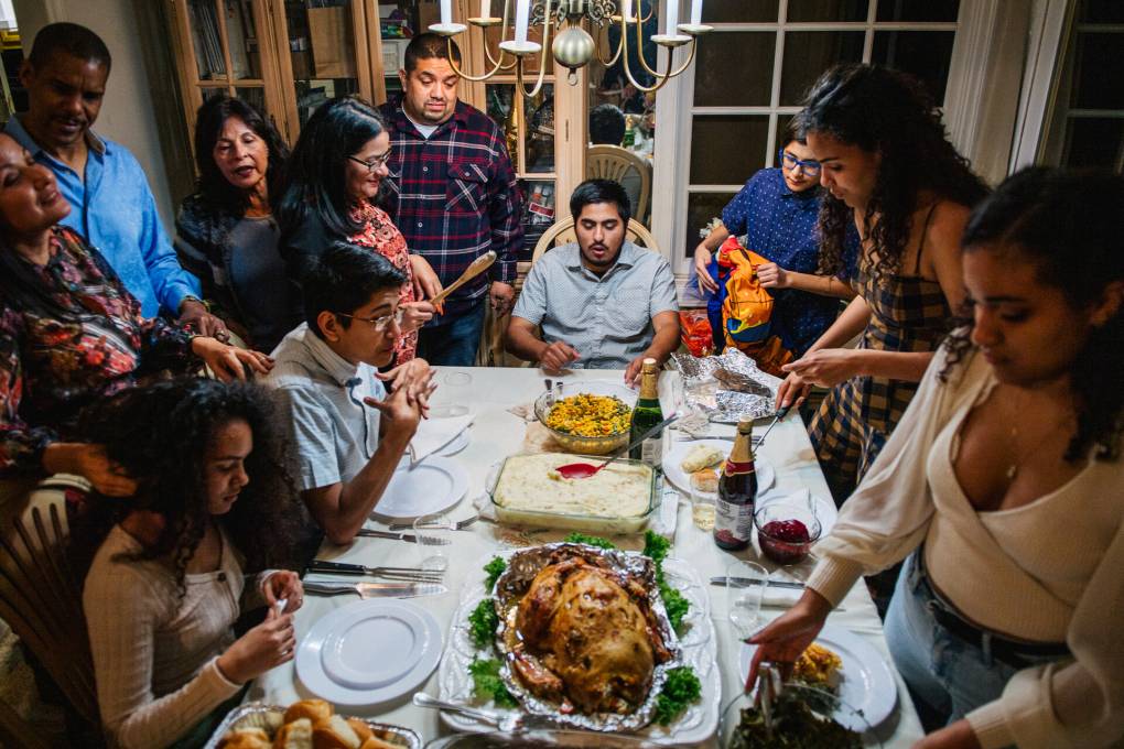 Family members stand around a table with many Thanksgiving dishes.