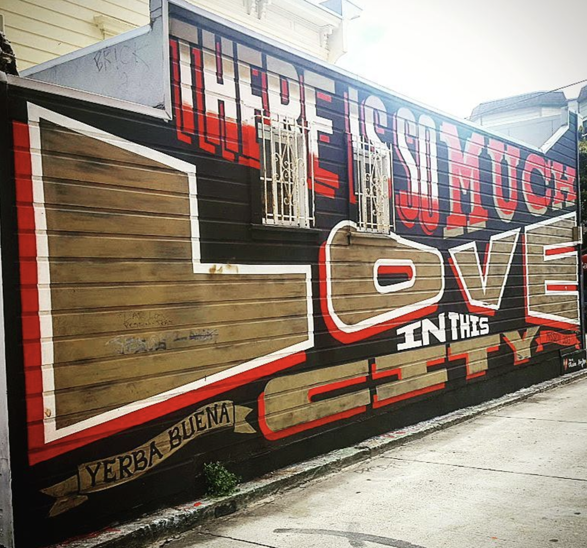 A gold, black and red mural that reads 'There is so much love in this city.'