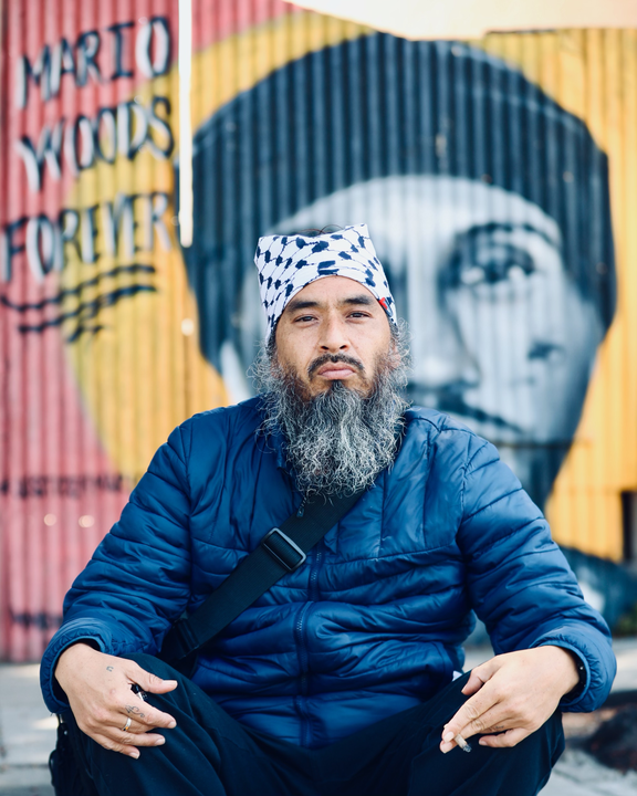 Rapper and political activist Equipto sits in front of a mural dedicated to Mario Woods, who was killed by SFPD in 2015.